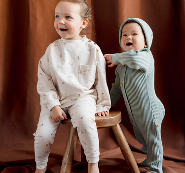 Picture shows little girl sitting on stool and baby boy wearing organic cotton rib knit beanie in jade color.