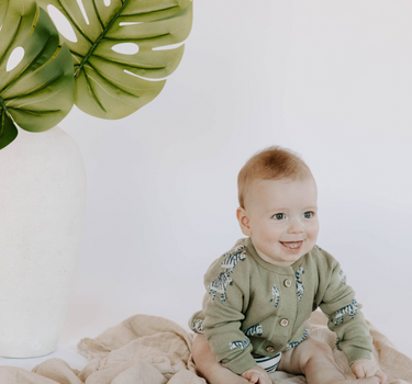 Baby boy wearing organic cotton knit cardigan in sage green with jacquard zebra pattern and magnetic button closures.