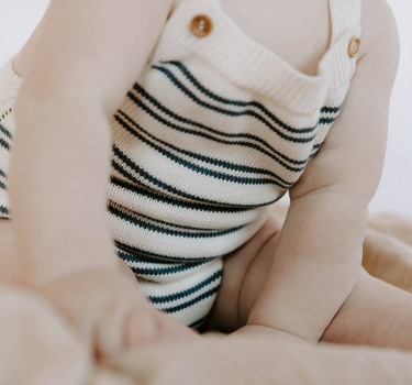 Baby wearing organic cotton stripe knit bubble romper in midnight stripes with magnetic closures at the crotch. 