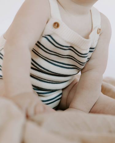 Baby wearing organic cotton stripe knit bubble romper in midnight stripes with magnetic closures at the crotch.
