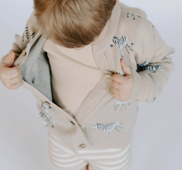 Little boy wearing organic cotton knit cardigan in mushroom beige with jacquard zebra pattern and magnetic button closures.