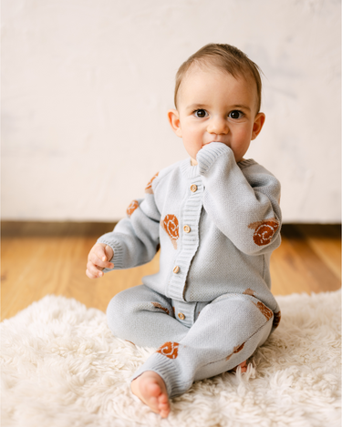 Image shows baby boy wearing organic cotton knit romper with snail jacquard pattern in pearl blue.