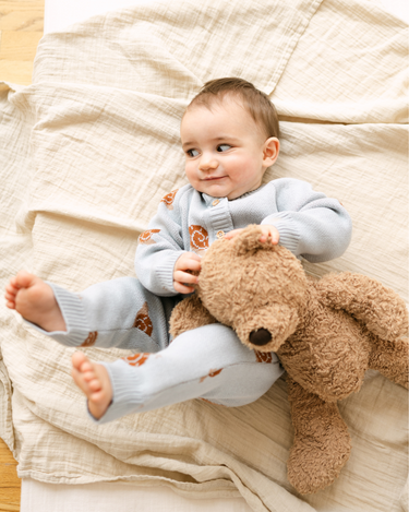 Image shows baby boy wearing organic cotton knit romper with snail jacquard pattern in pearl blue.