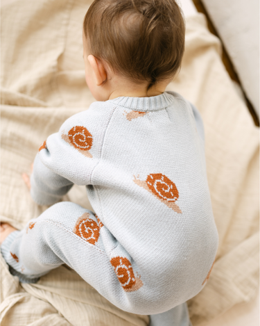 Image shows baby boy wearing organic cotton knit romper with snail jacquard pattern in pearl blue.