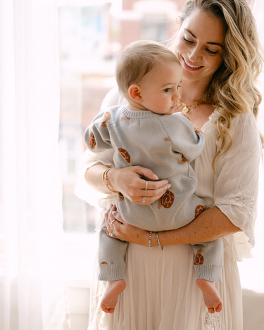 Image shows baby boy wearing organic cotton knit romper with snail jacquard pattern in pearl blue.