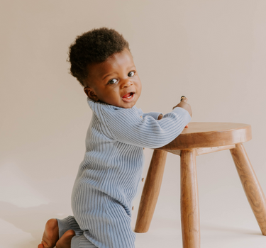 Baby boy kneeling wearing organic cotton rib knit romper with Magnetic Buttons for easy changes in stormy blue color.