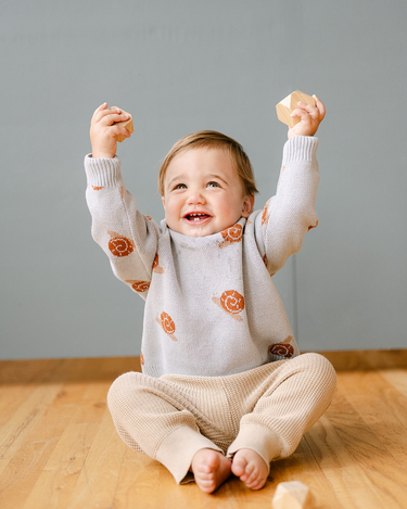 Image shows baby boy wearing organic cotton knit sweater with jacquard snail pattern in pearl blue.