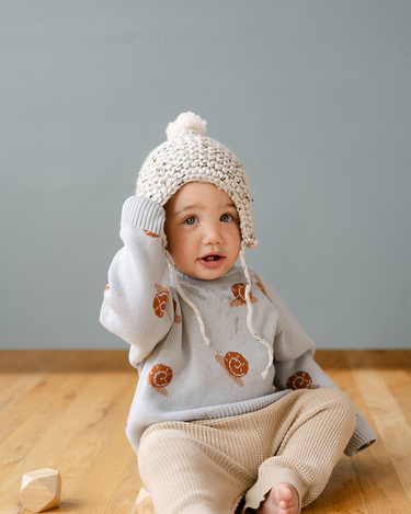 Image shows baby boy wearing organic cotton knit sweater with jacquard snail pattern in pearl blue.