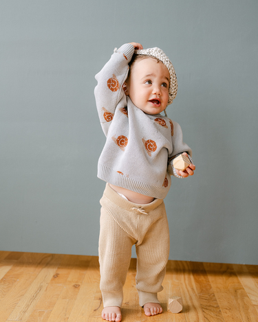 Image shows baby boy wearing organic cotton knit sweater with jacquard snail pattern in pearl blue.