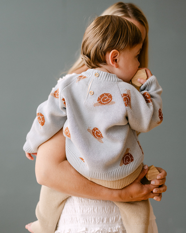 Image shows baby boy wearing organic cotton knit sweater with jacquard snail pattern in pearl blue.
