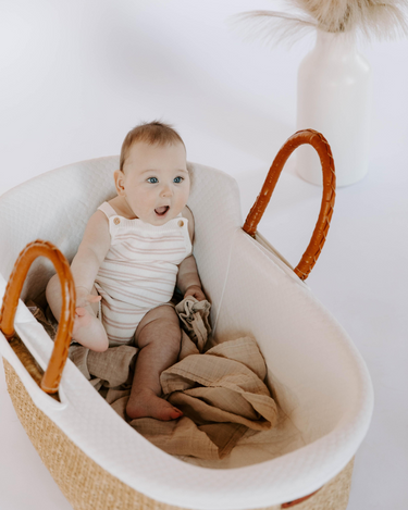 Image shows baby girl sitting in bassinet wearing organic cotton stripe knit romper in orchid pink stripes.