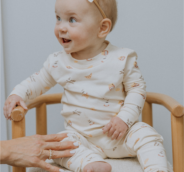 Baby wearing modal pajama set in Petit Déjeuner print with coffee mugs, croissants, butter, and jam.