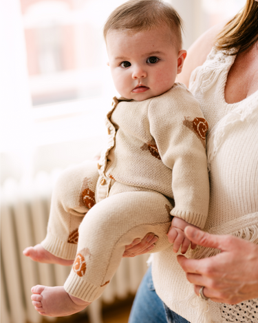 Image shows baby girl wearing organic cotton knit romper with jacquard snail pattern in oatmeal color.