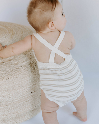 Baby girl standing wearing organic cotton knit romper in mushroom stripes.