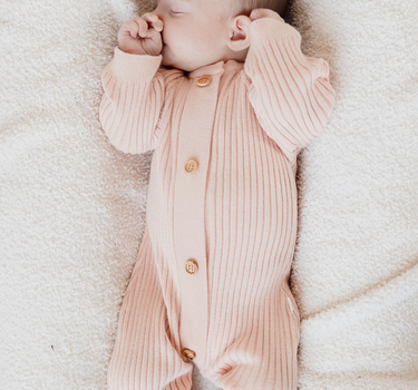 Photo shows baby girl wearing organic cotton knit romper in raspberry macaron with Magnetic Buttons.