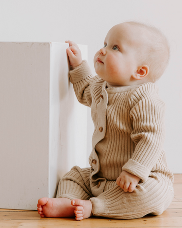 Photo shows baby girl sitting wearing sandcastle organic cotton knit romper with Magnetic Buttons.
