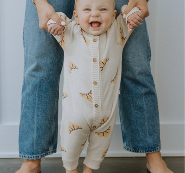 Baby wearing organic cotton knit croissant patterned romper with Magnetic Button closures.