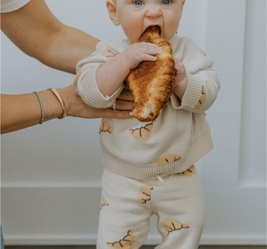 Baby wearing organic cotton knit croissant patterned joggers and matching sweater.