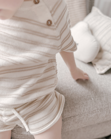 Image shows close up shot of toddler girl wearing organic cotton stripe knit set in mushroom.