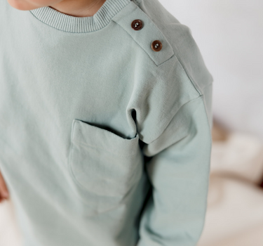 Image shows little boy wearing Organic Cotton Italian Fleece sweatshirt in jade with Magnetic Buttons at neck.