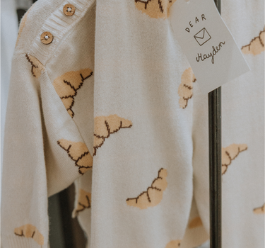 Organic cotton knit croissant patterned joggers and matching sweater hanging from hangers.