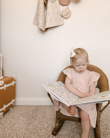 Little girl sitting in chair wearing organic cotton muslin flutter sleeve dress in orchid pink.