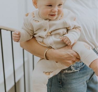 Baby wearing organic cotton knit croissant patterned romper with Magnetic Button closures.