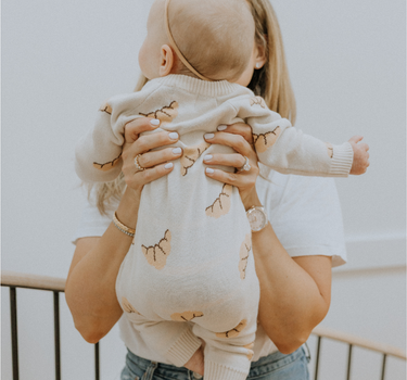 Baby wearing organic cotton knit croissant patterned romper with Magnetic Button closures.