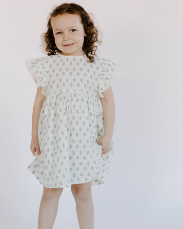 Image shows little girl wearing organic cotton muslin flutter sleeve dress in cheerful floral.