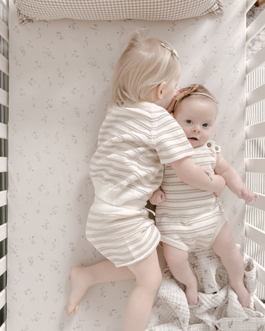 Image shows siblings cuddling in crib wearing organic cotton stripe knit set in mushroom and stripe romper in mushroom.