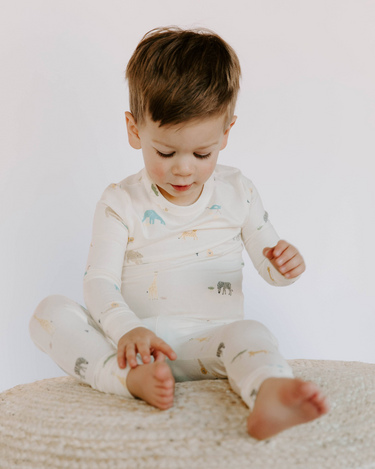 Image shows toddler boy sitting wearing modal pajama set in zoo print.