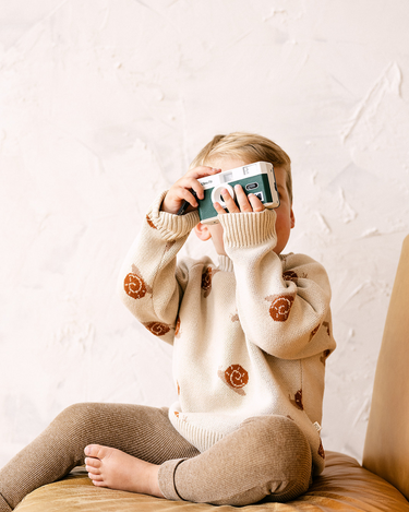 Image shows toddler boy wearing organic cotton knit sweater with snail jacquard pattern in oatmeal.