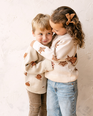 Image shows toddler boy wearing organic cotton knit sweater with snail jacquard pattern in oatmeal.