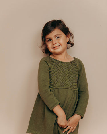 Image of little girl wearing knit dress in crocodile color with sweet details and button detail at the back of the neck.