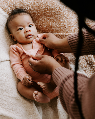 Baby girl wearing organic cotton rib bodysuit with Magnetic Buttons for easy changing in strawberries and cream color. Bodysuit opens with Magnetic Buttons at the neck as well as crotch.