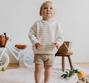 Image of little boy wearing organic cotton knit shorts in sandcastle color with faux drawstrings. 