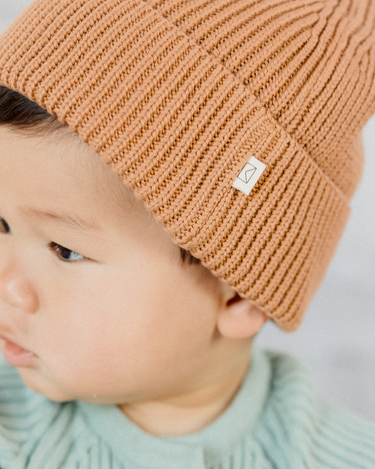 Picture shows baby boy wearing organic cotton rib knit beanie in Acorn color. 