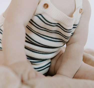 Baby wearing organic cotton stripe knit bubble romper in midnight stripes with magnetic closures at the crotch.