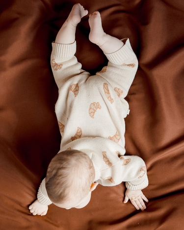 Image shows baby girl wearing organic cotton knit croissant romper.