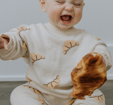 Baby girl wearing organic cotton knit croissant patterned sweater with Magnetic Button closures at the neck and matching knit joggers.