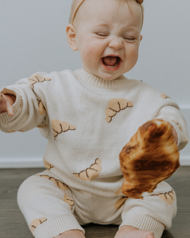 Baby girl wearing organic cotton knit croissant patterned sweater with Magnetic Button closures at the neck and matching knit joggers.