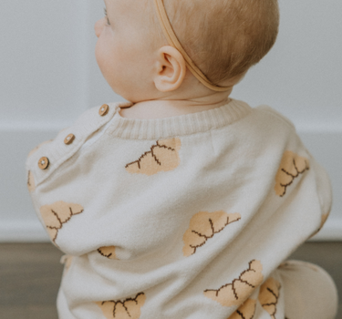 Baby girl wearing organic cotton knit croissant patterned sweater with Magnetic Button closures at the neck.