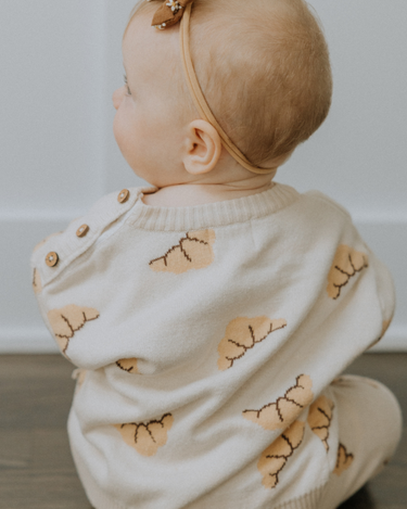 Baby girl wearing organic cotton knit croissant patterned sweater with Magnetic Button closures at the neck. 