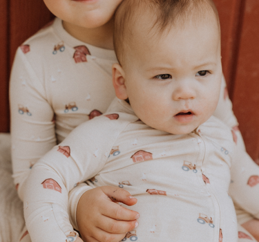 picture of baby boy wearing modal convertible footy pajamas in light beige color with farm print