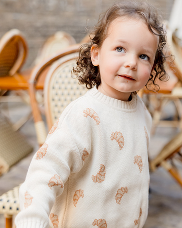 Little girl looking up while wearing organic cotton knit croissant jacquard pattern sweater with Magnetic Buttons at the shoulder.
