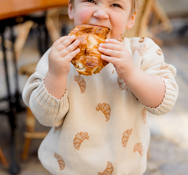 Image shows toddler boy wearing organic cotton knit croissant sweater and organic cotton modal rib leggings in acorn. 