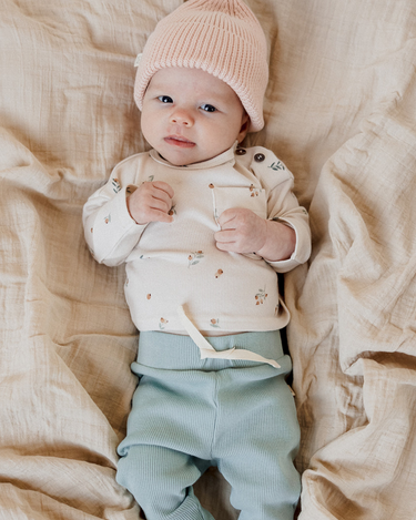 Picture shows baby girl wearing organic cotton modal rib long sleeve tee in floral bud with magnetic buttons at neck.