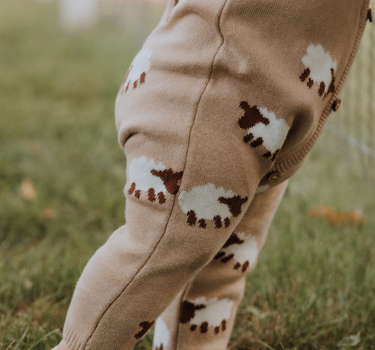 baby wearing organic cotton beige romper with sheep jacquard pattern and magnetic buttons from neck to crotch