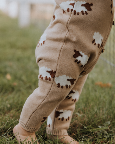 baby wearing organic cotton beige romper with sheep jacquard pattern and magnetic buttons from neck to crotch