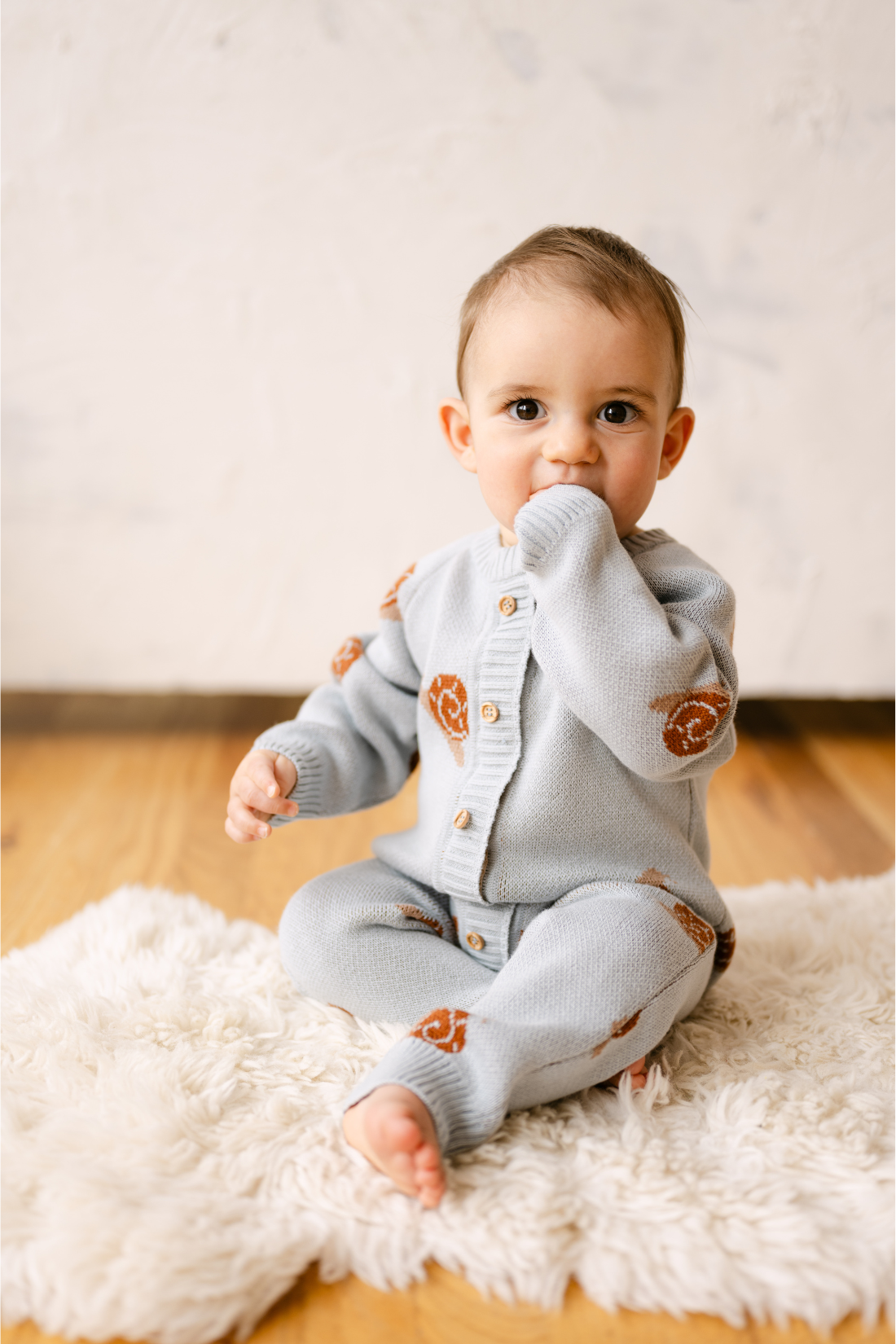 Image shows baby boy wearing organic cotton knit romper with snail jacquard pattern in pearl blue. 